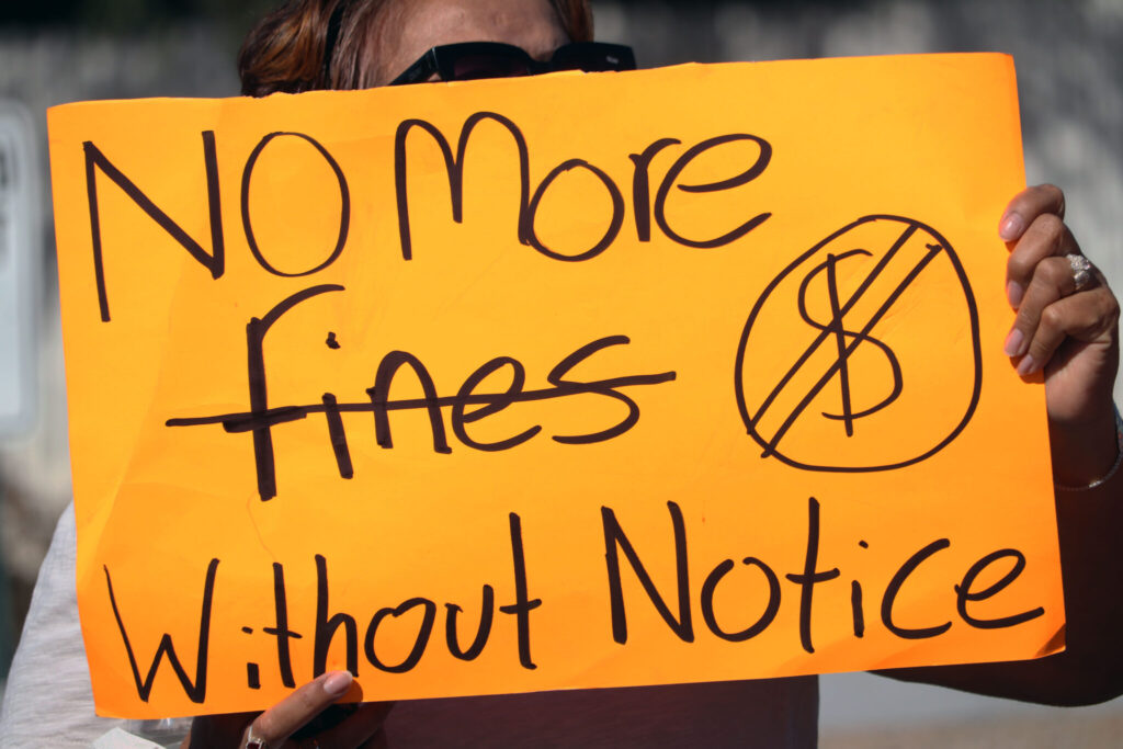 Woman holding sign that says "No More Fines without Notice"